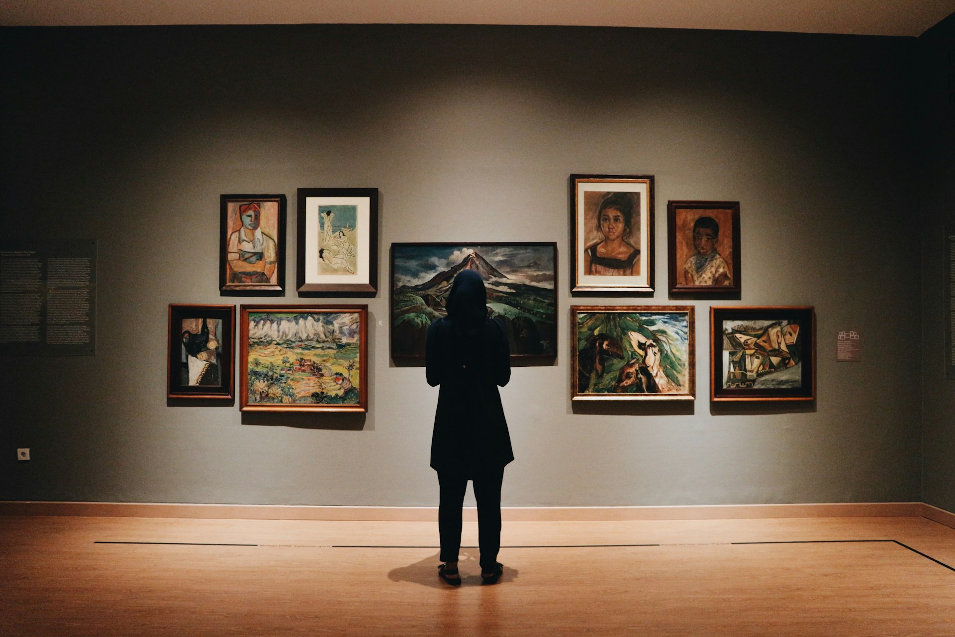 A visitor viewing a wall of paintings in an art gallery